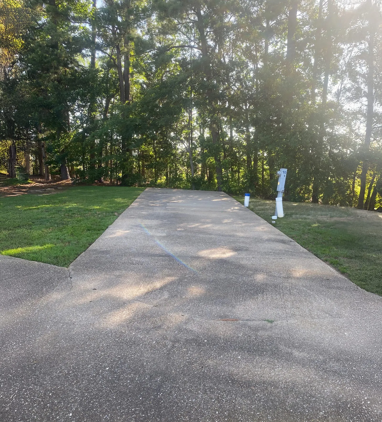 A back-in concrete RV site bordered by lawn and pine trees