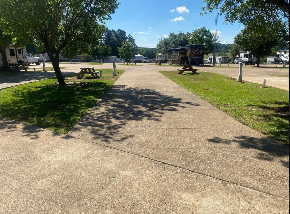 A pull-through concrete RV site with grass and shade trees on either side
